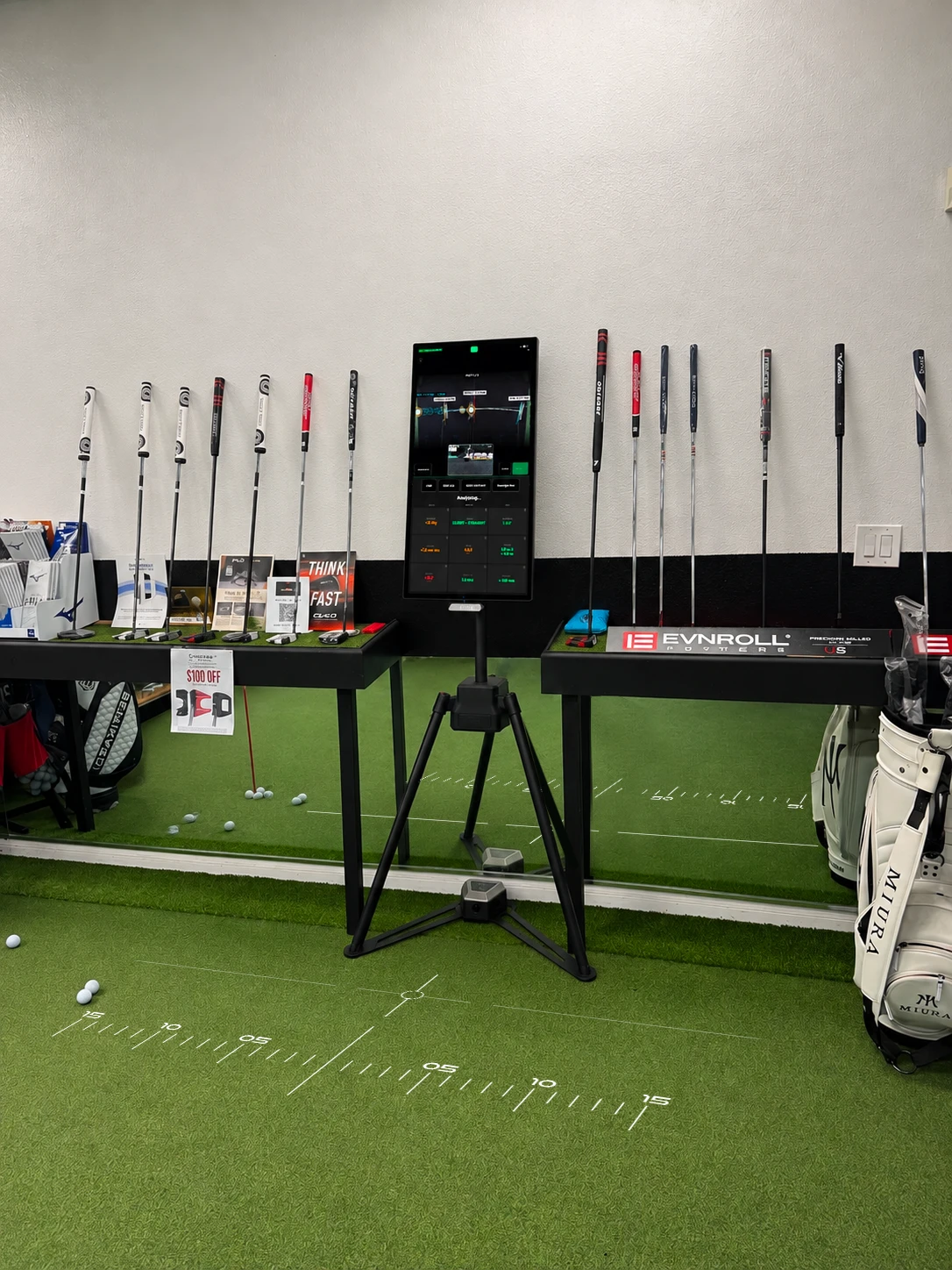 Putter Experience on its stand in a pro shop, between the putter racks